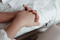 Close-up of two hands holding on a bed, symbolizing intimacy and support.