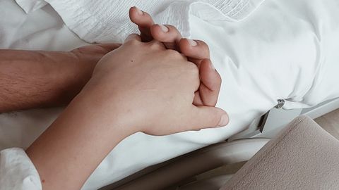 Close-up of two hands holding on a bed, symbolizing intimacy and support.