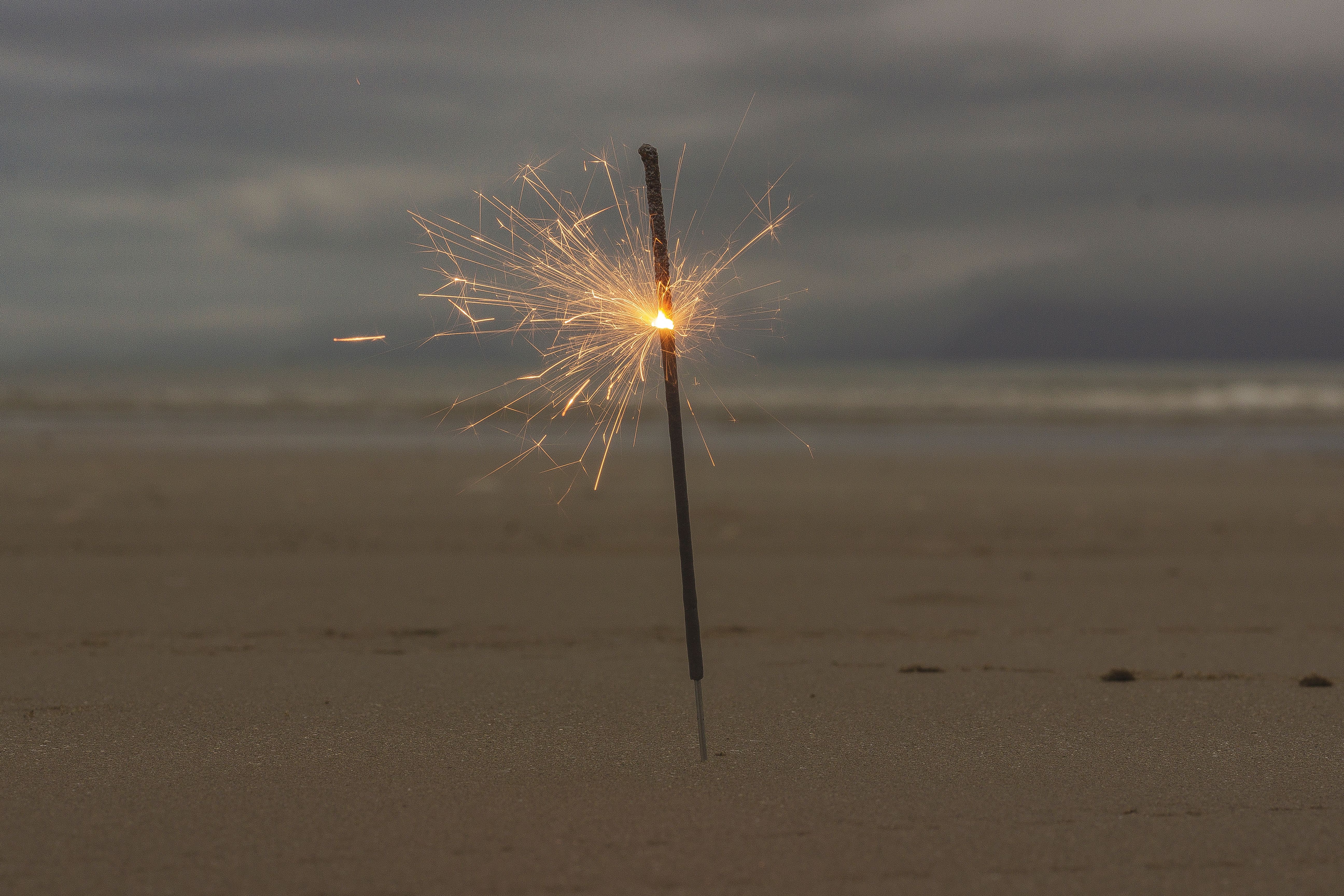 A glowing sparkler shines brightly on an empty beach at dusk, creating a festive atmosphere.