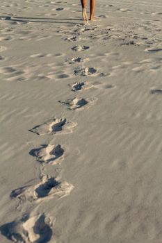 Bare feet leaving footprints on a tranquil sandy beach during sunset, conveying a peaceful vacation vibe.
