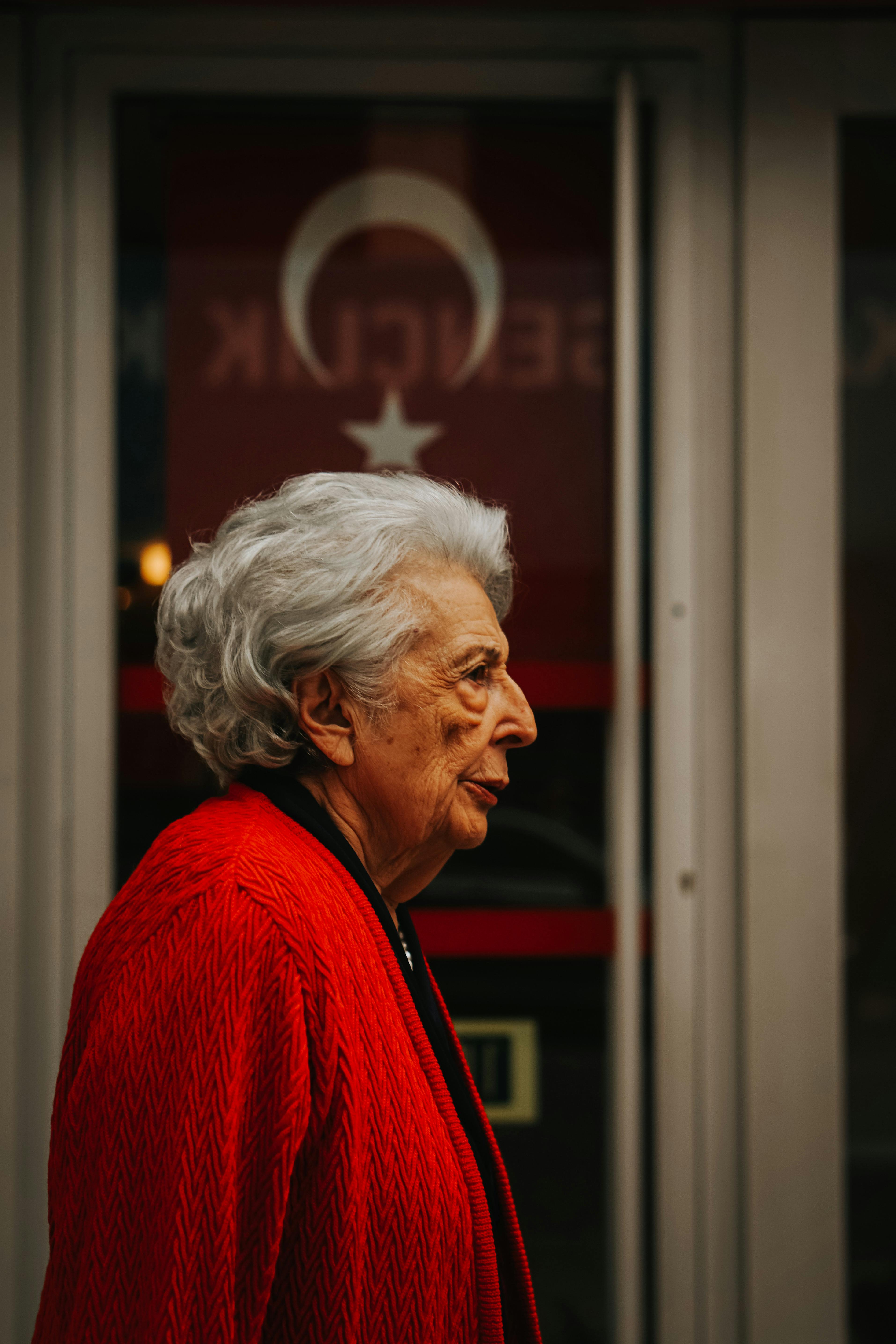 Elderly woman in Ankara with a backdrop of Turkish flag elements, symbolizing heritage and culture.