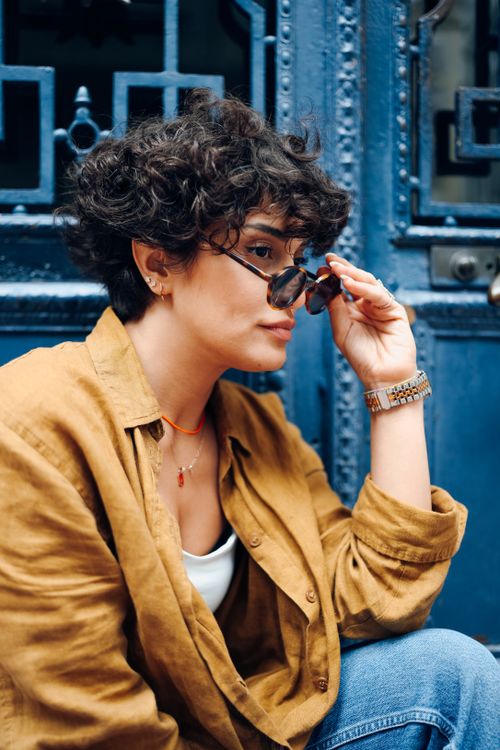 Free A fashionable adult wearing sunglasses sits against a decorative blue door, embodying urban street style. Stock Photo