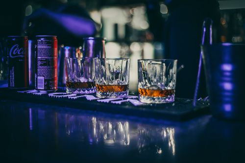 Free Chilled whiskey glasses on a dimly lit bar counter with soda cans in the background. Stock Photo