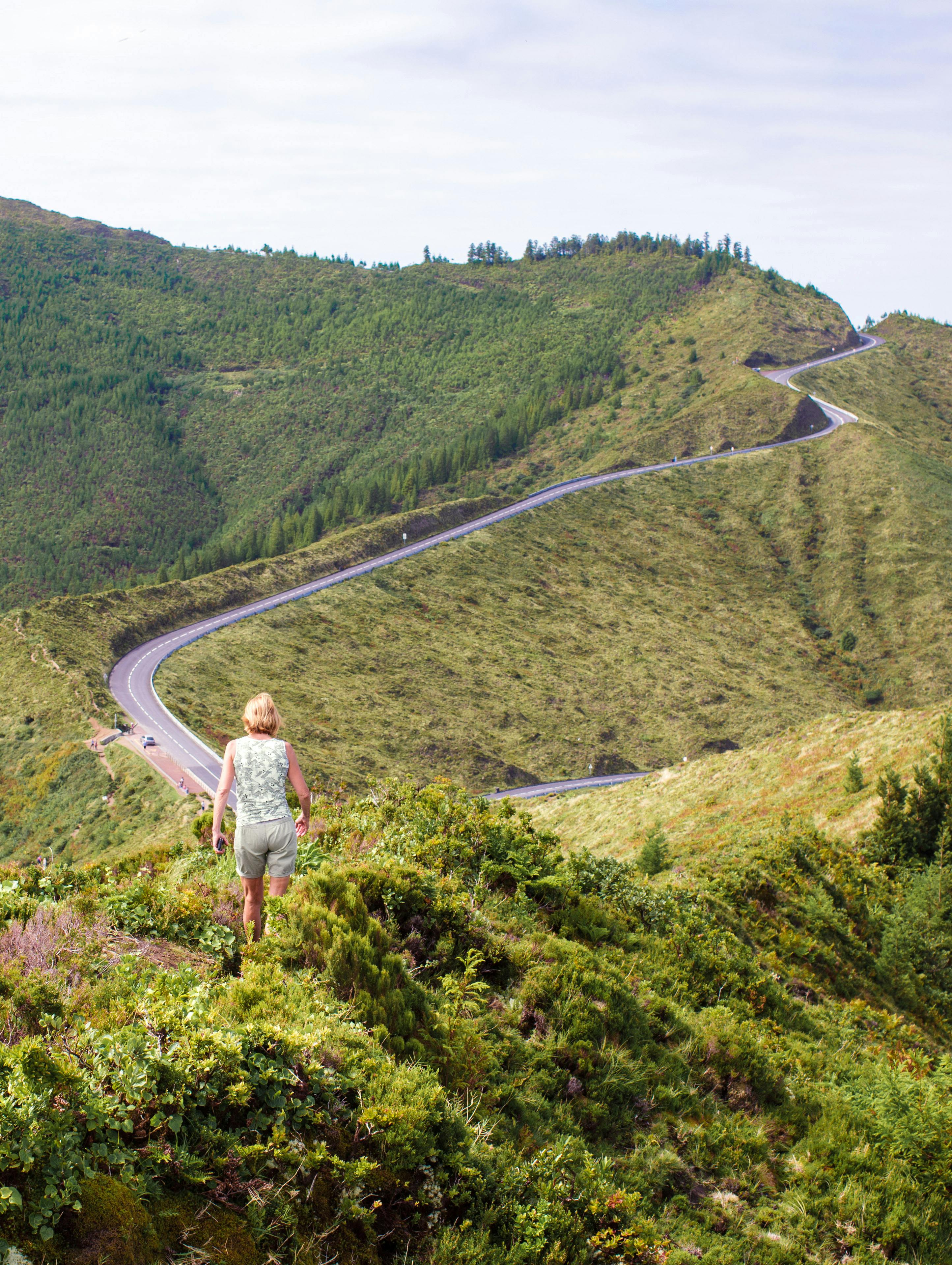 Woman hiking in lush landscape with winding road in Ponta Delgada, Azores, Portugal.