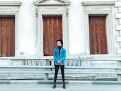 一位穿着牛仔夹克、戴着太阳镜的时尚男子，自信地站在历史建筑上