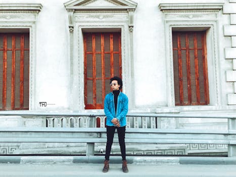 一位穿着牛仔夹克、戴着太阳镜的时尚男子，自信地站在历史建筑上