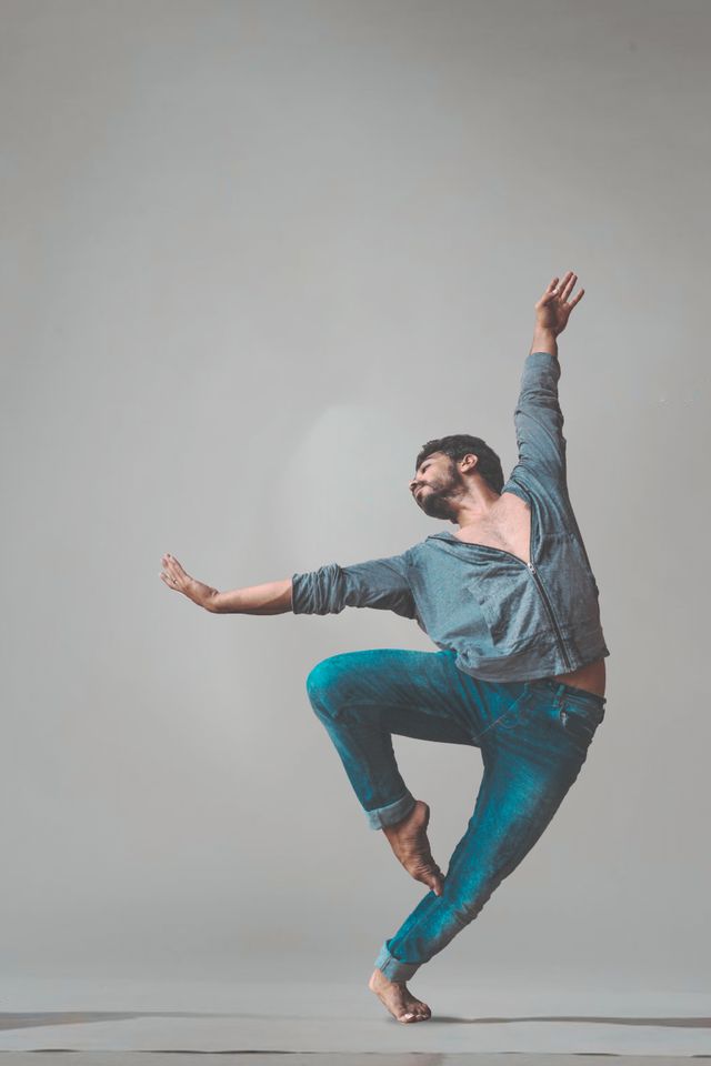 Bailarín en un gesto de giro con un brazo en alto, sobre fondo claro