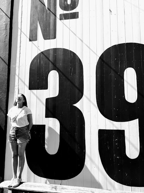 Grayscale Photo Of Woman Standing Beside White And Black Wall