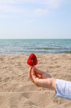 Woman's hand holding a strawberry against a calm seaside backdrop.