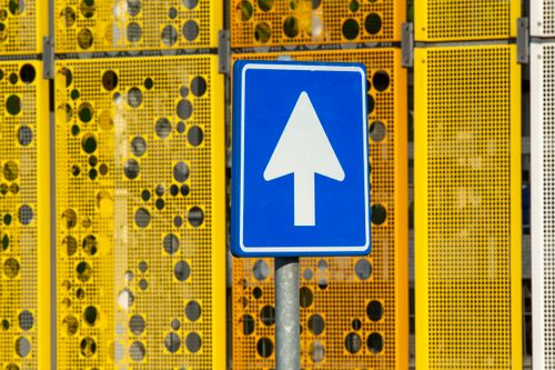 Free Blue traffic sign with upward arrow on a sunny day, vibrant yellow background. Stock Photo