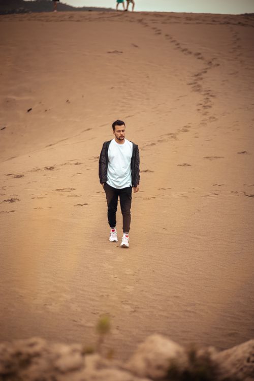 Free A man leisurely strolls across sandy dunes, epitomizing relaxation and adventure. Stock Photo