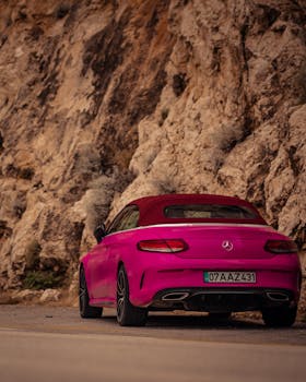 Bright pink car driving on a rocky mountain road providing a vivid contrast.