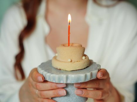 A woman's hands holding a small birthday cake with a lit candle, celebrating a special occasion.