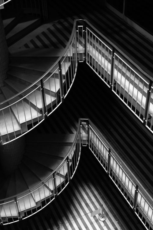 Free A dramatic black and white photograph of a modern spiral staircase with geometric patterns in shadows. Stock Photo