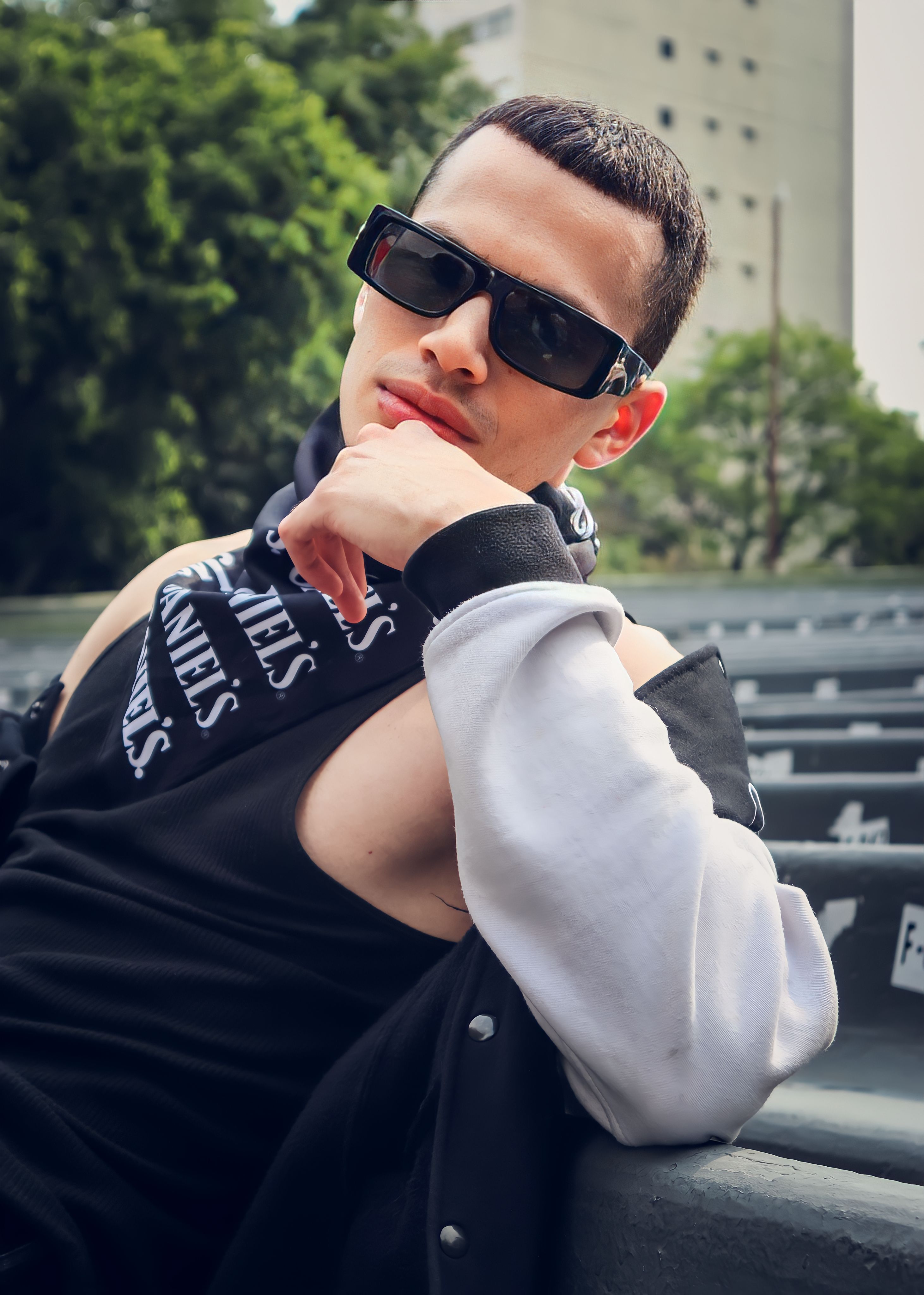 Fashionable man wearing sunglasses and sportswear poses confidently on a sunny day.