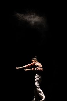 A captivating dancer performs under a dramatic spotlight with smoke effects on a dark stage.