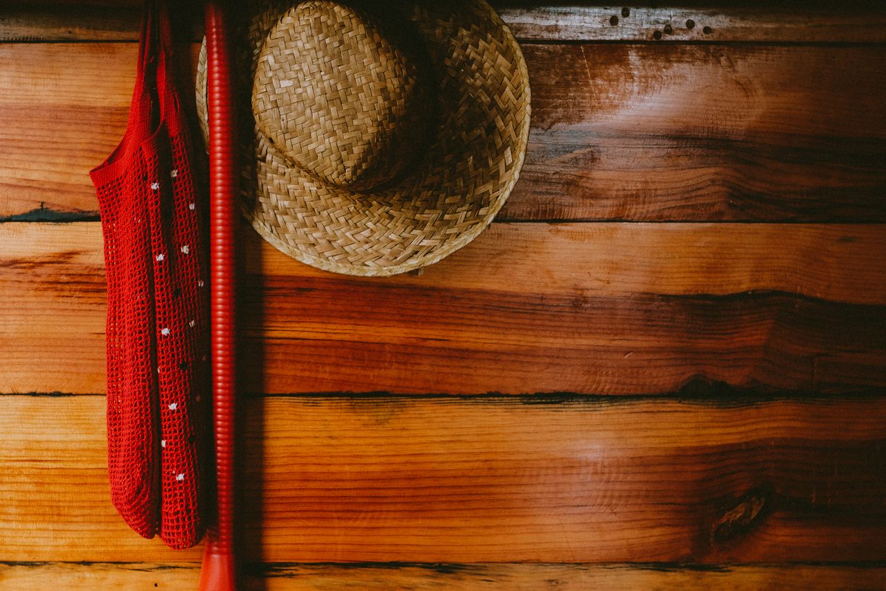 a straw hat and red cloth hang on a rustic wooden wall creating a cozy