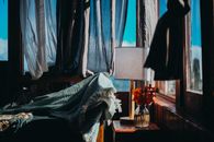 A cozy bedroom scene featuring sunlight streaming through curtains, a blanket, and a vase of flowers.