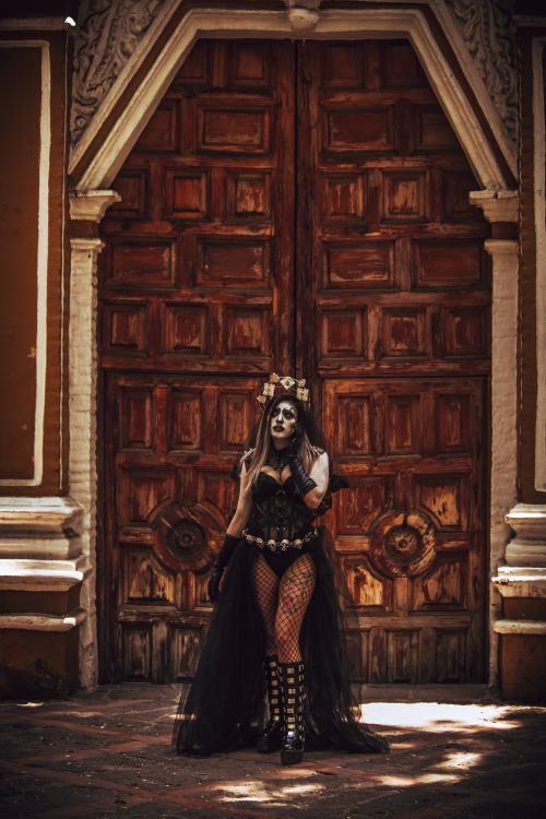 Free A woman in traditional Dia de Muertos attire stands before an ornate wooden door, embodying Mexican culture. Stock Photo