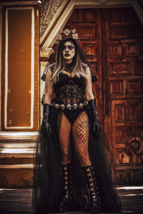 Free Woman with painted face and black dress standing in front of ornate wooden door, celebrating Dia de Muertos. Stock Photo