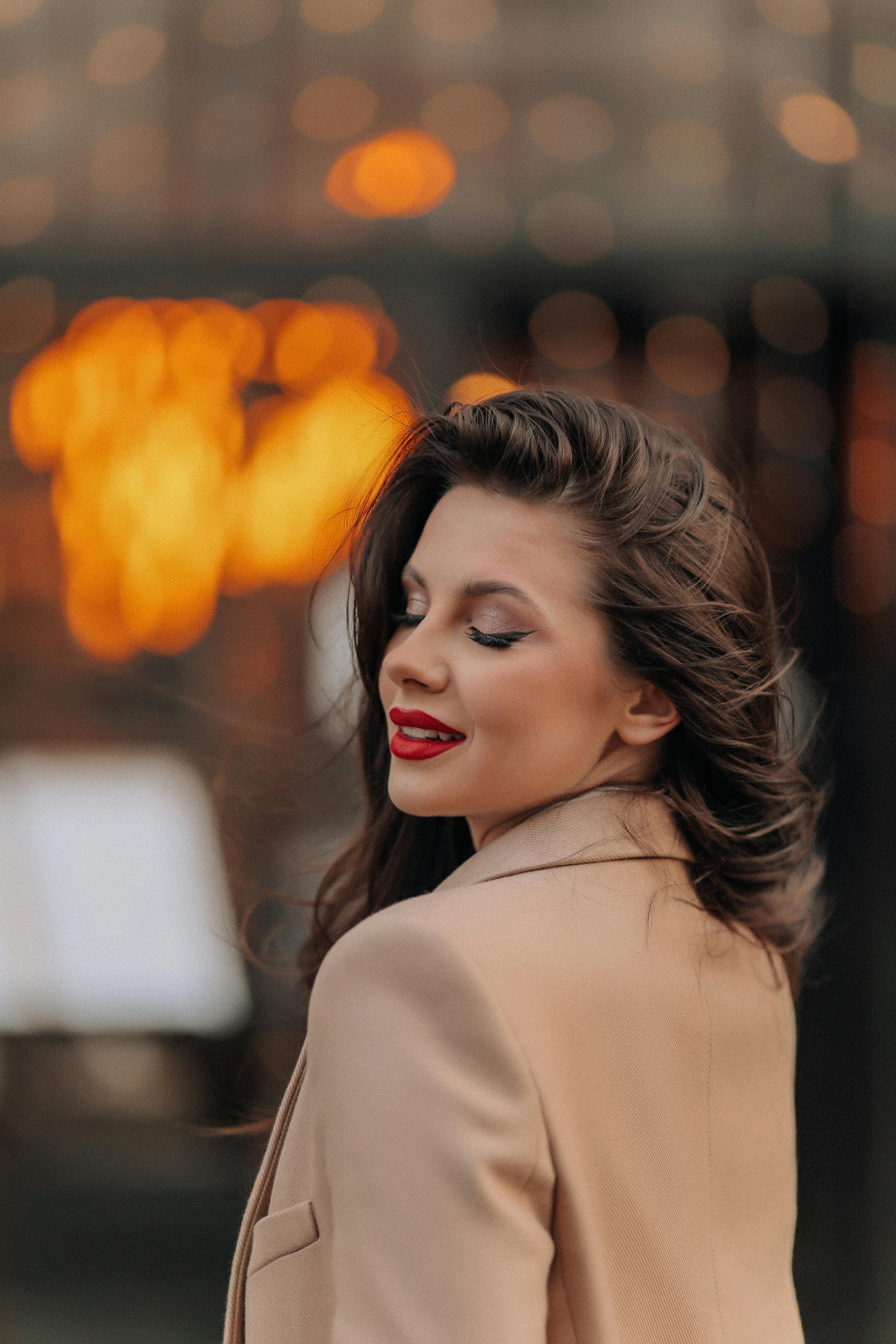Free Sophisticated woman with closed eyes in a stylish coat against city lights bokeh background. Stock Photo