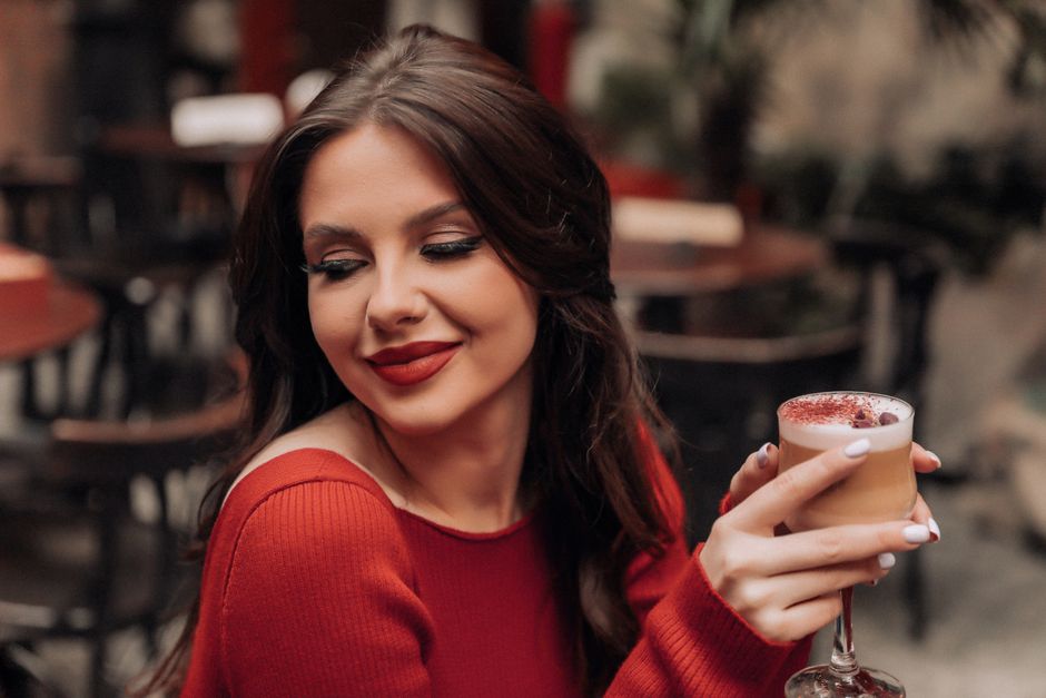 A stylish woman in a red dress savoring a cappuccino in a cozy cafe setting.