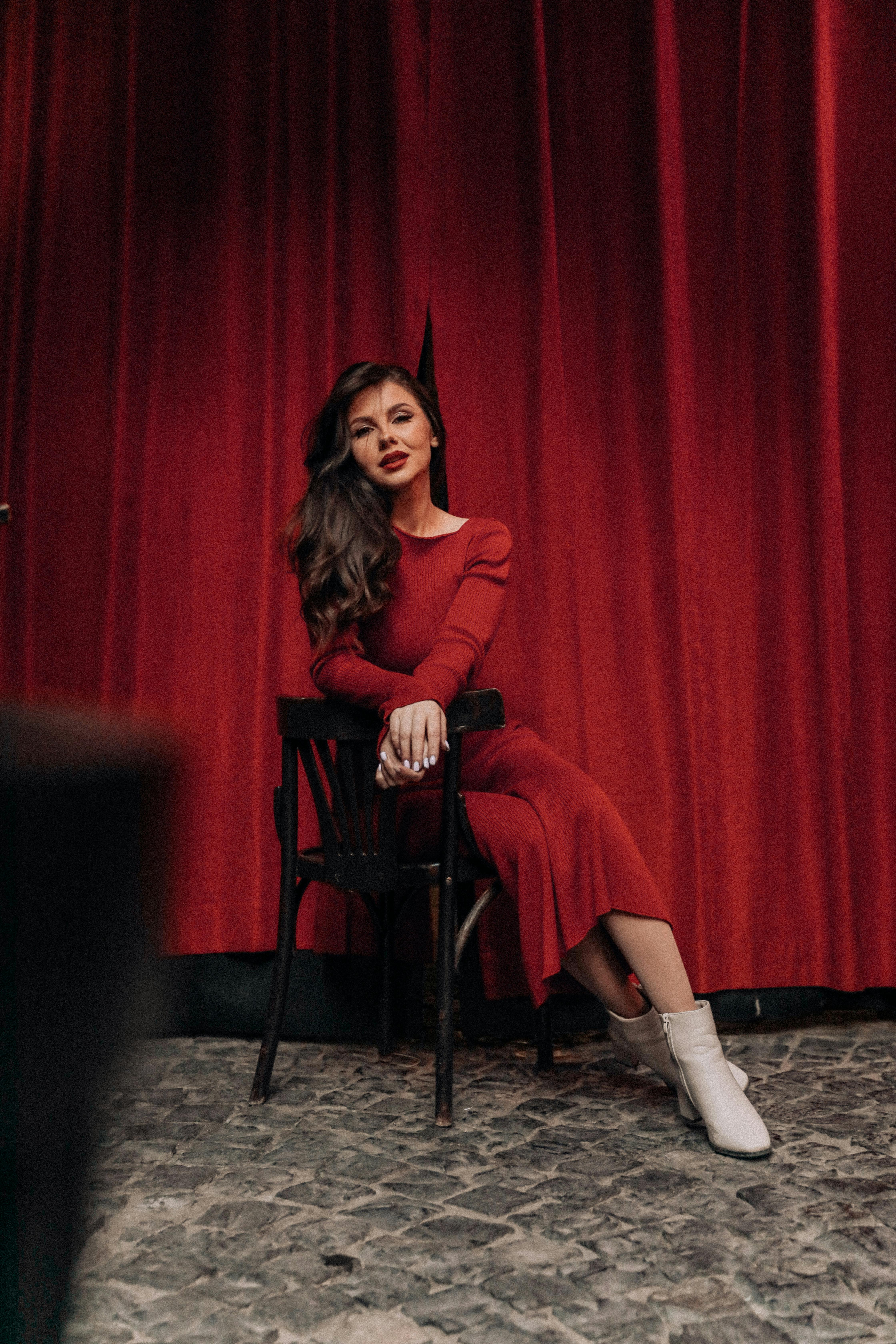 Free Sophisticated woman in a red dress posing indoors with red curtains. Stock Photo