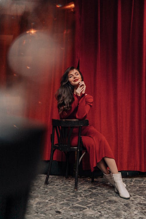 Woman in a Red Dress Sitting on a Chair in front of a Red Curtain 