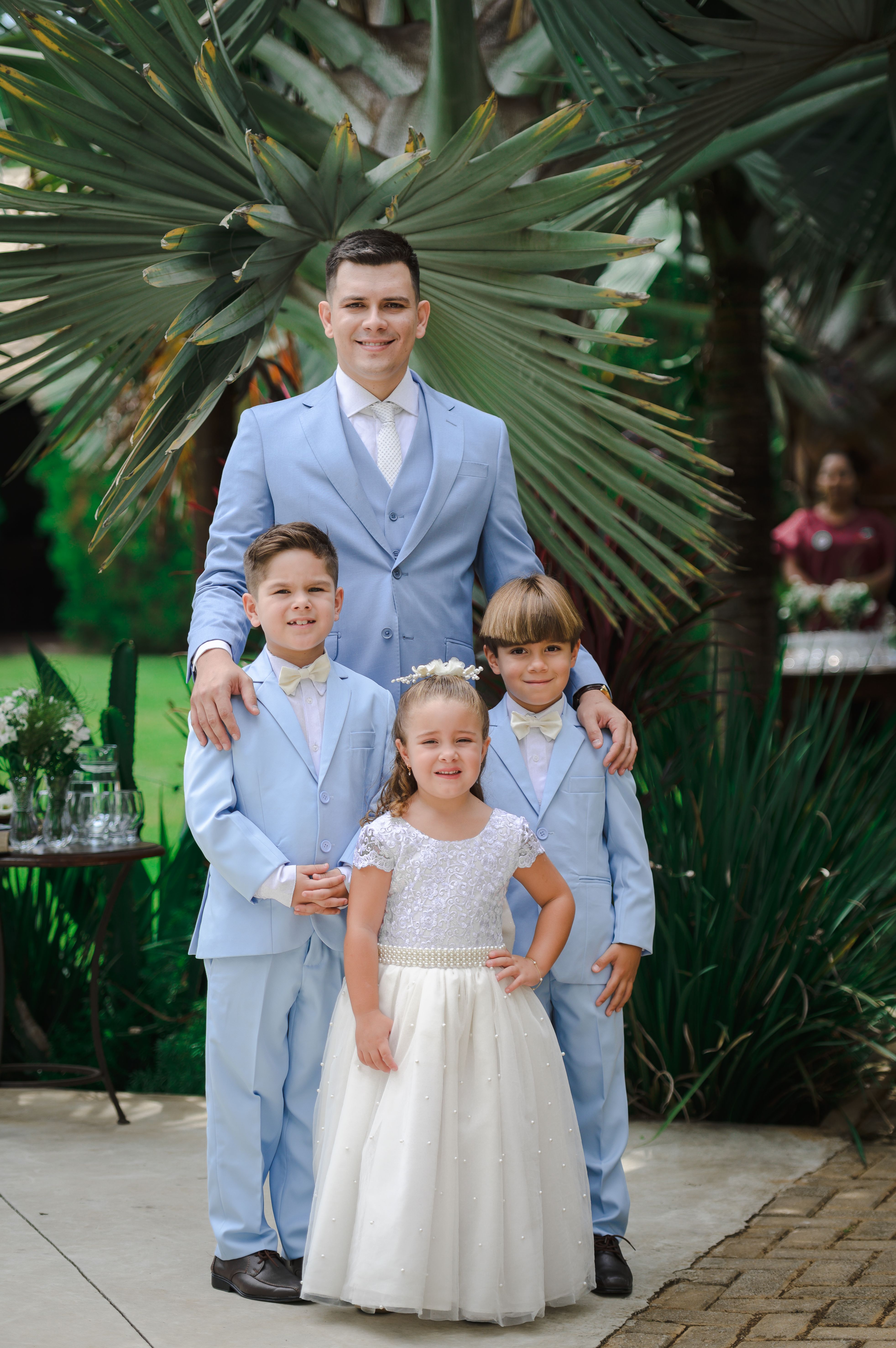 Family portrait of a father with three children in formal attire at an outdoor wedding setting.