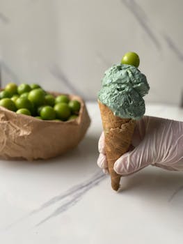 A delicate hand holds a unique green ice cream cone garnished with a lime.