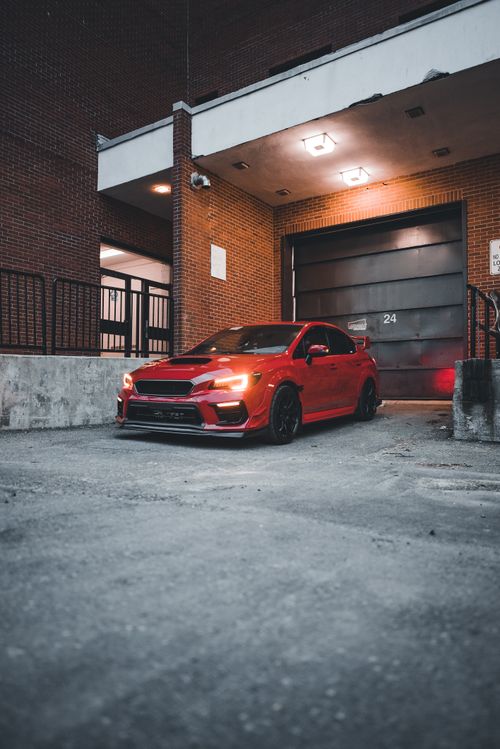 Free A striking red Subaru parked in a dimly-lit urban garage at night. Stock Photo