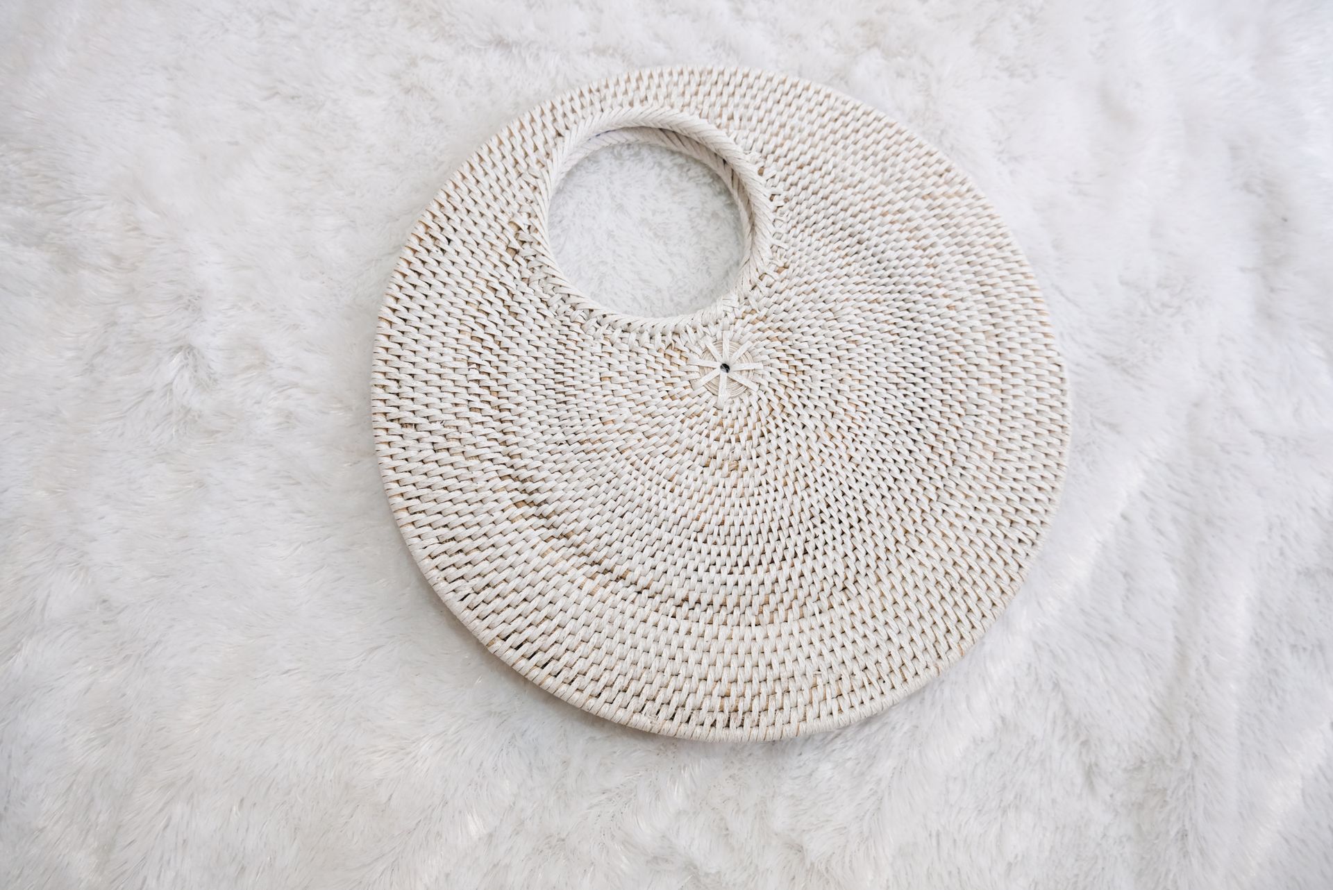 Elegant round woven handbag resting on a soft white fur surface, perfect for a chic look.