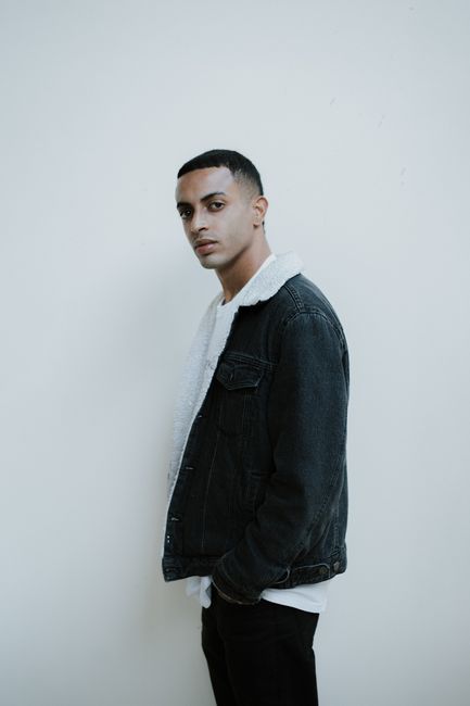 Stylish portrait of a man posing in a denim jacket, standing against a white background.