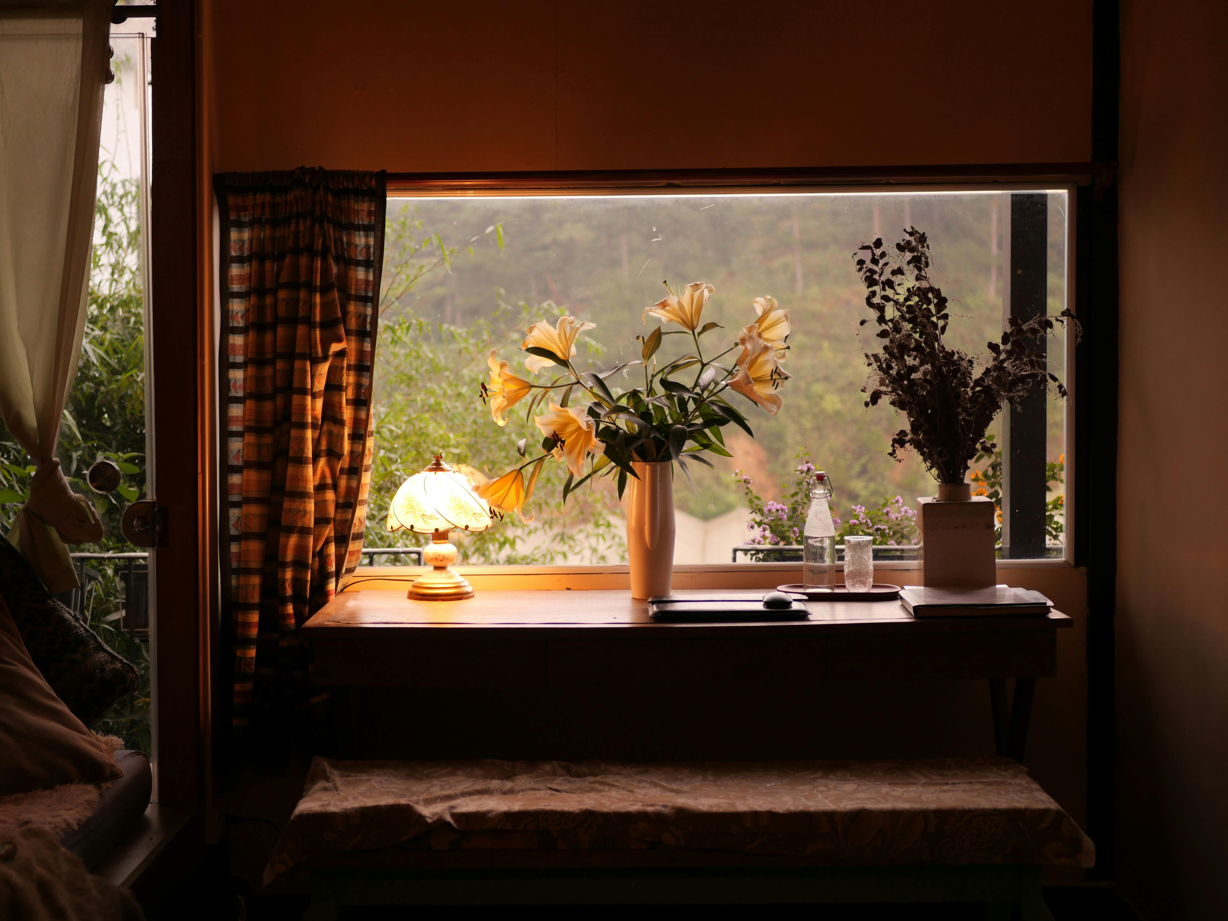A tranquil indoor scene with a table, flowers, and lamp by a window in Đà Lạt.