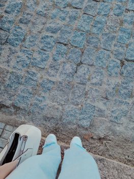 A top view of a woman's feet standing on cobblestones beside a bag.