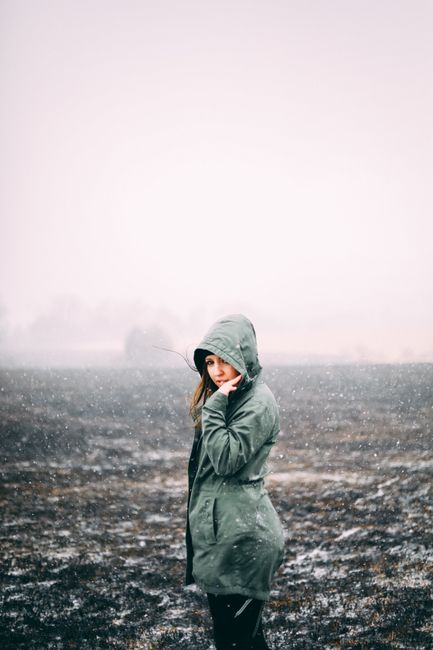 A young woman in a hooded coat stands alone in a foggy, snowy field, creating an atmospheric winter scene.