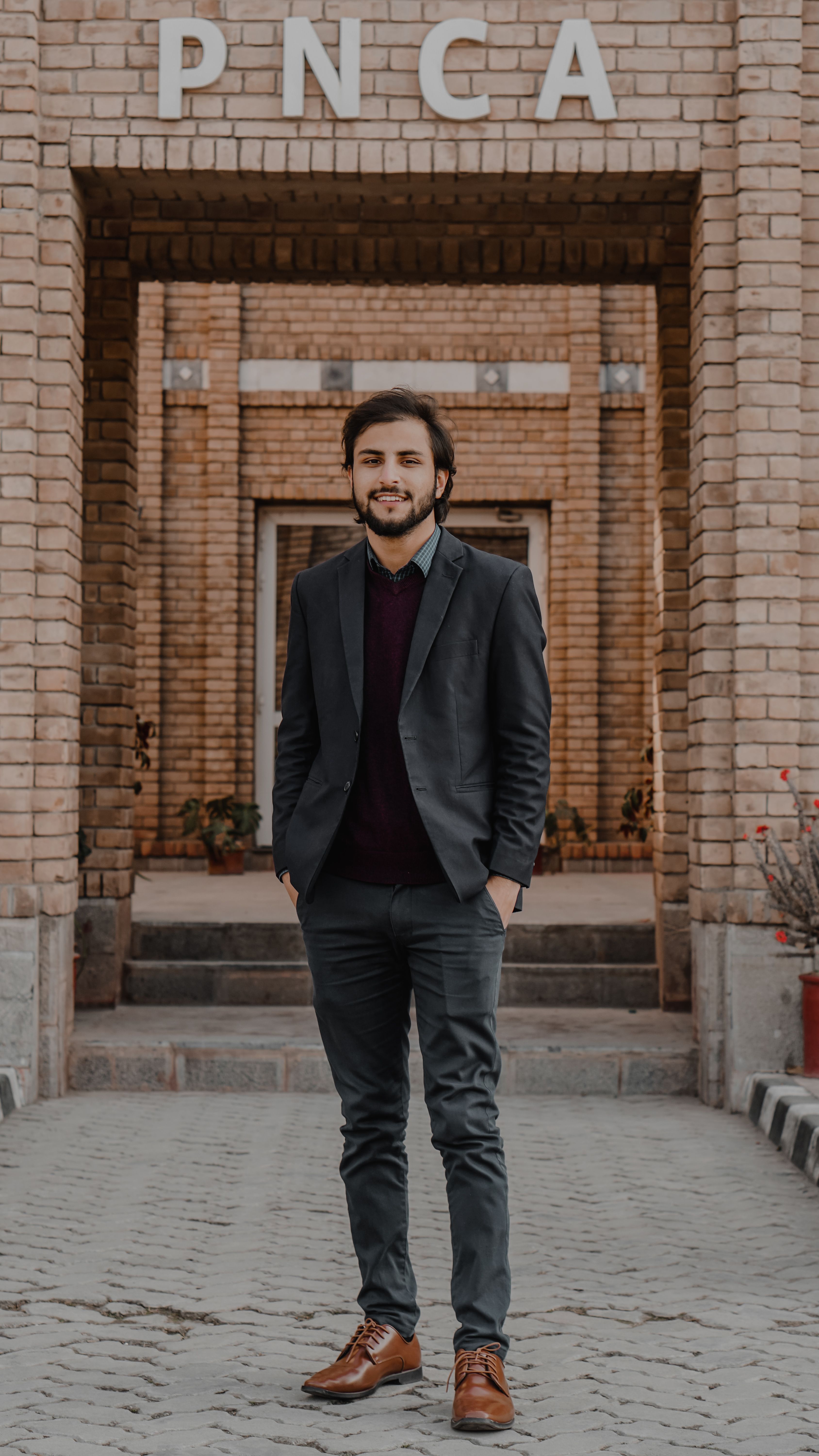 Smiling young man in formal attire posing confidently outside the brick facade of the PNCA building.