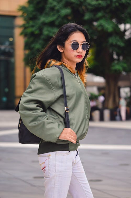 Woman in a Green Jacket and White Pants Walking in the City 