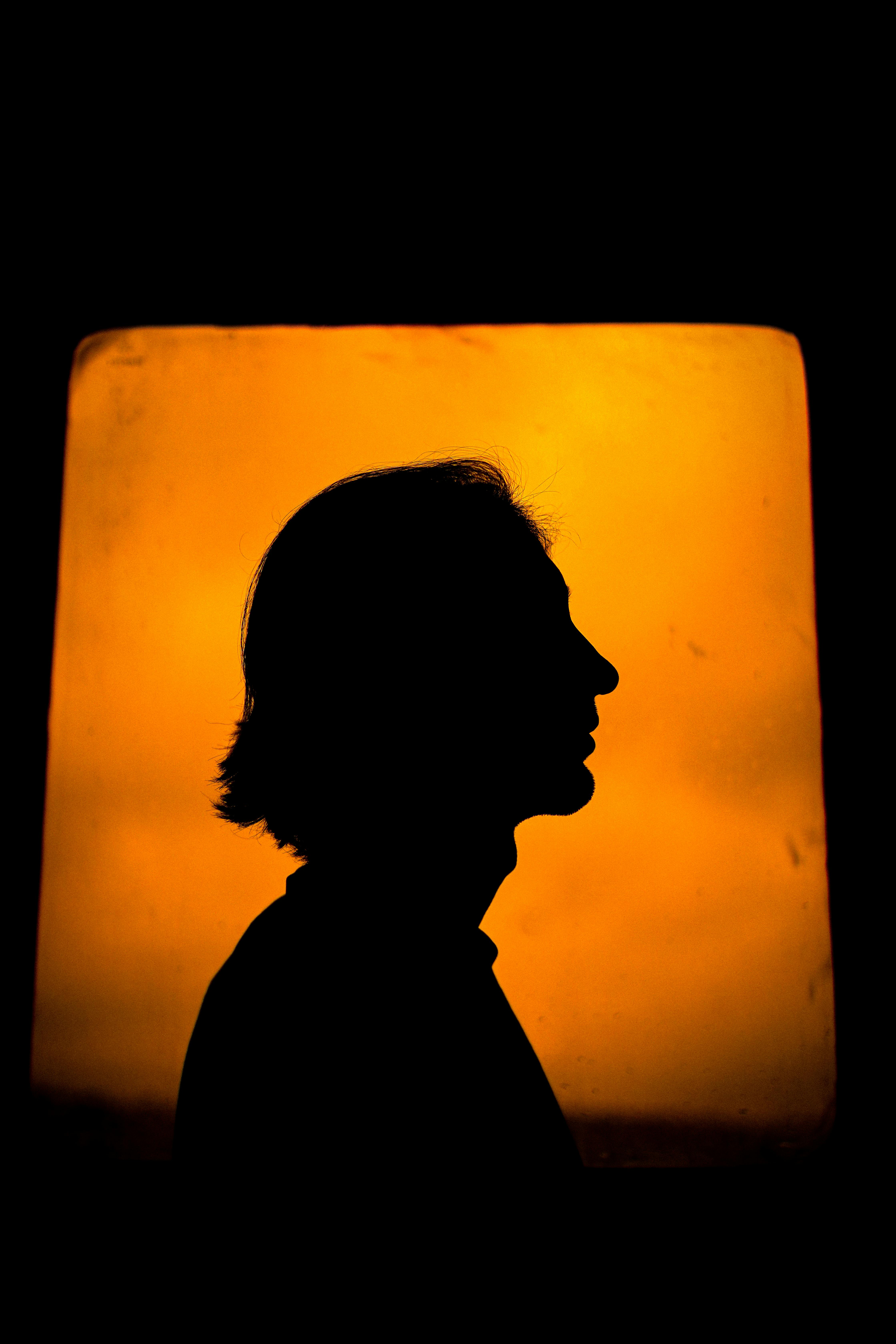 A striking silhouette profile of a person against a vivid orange backdrop, creating a dramatic mood.