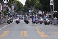 A police motorcade advances through a city street during a parade, with spectators watching.