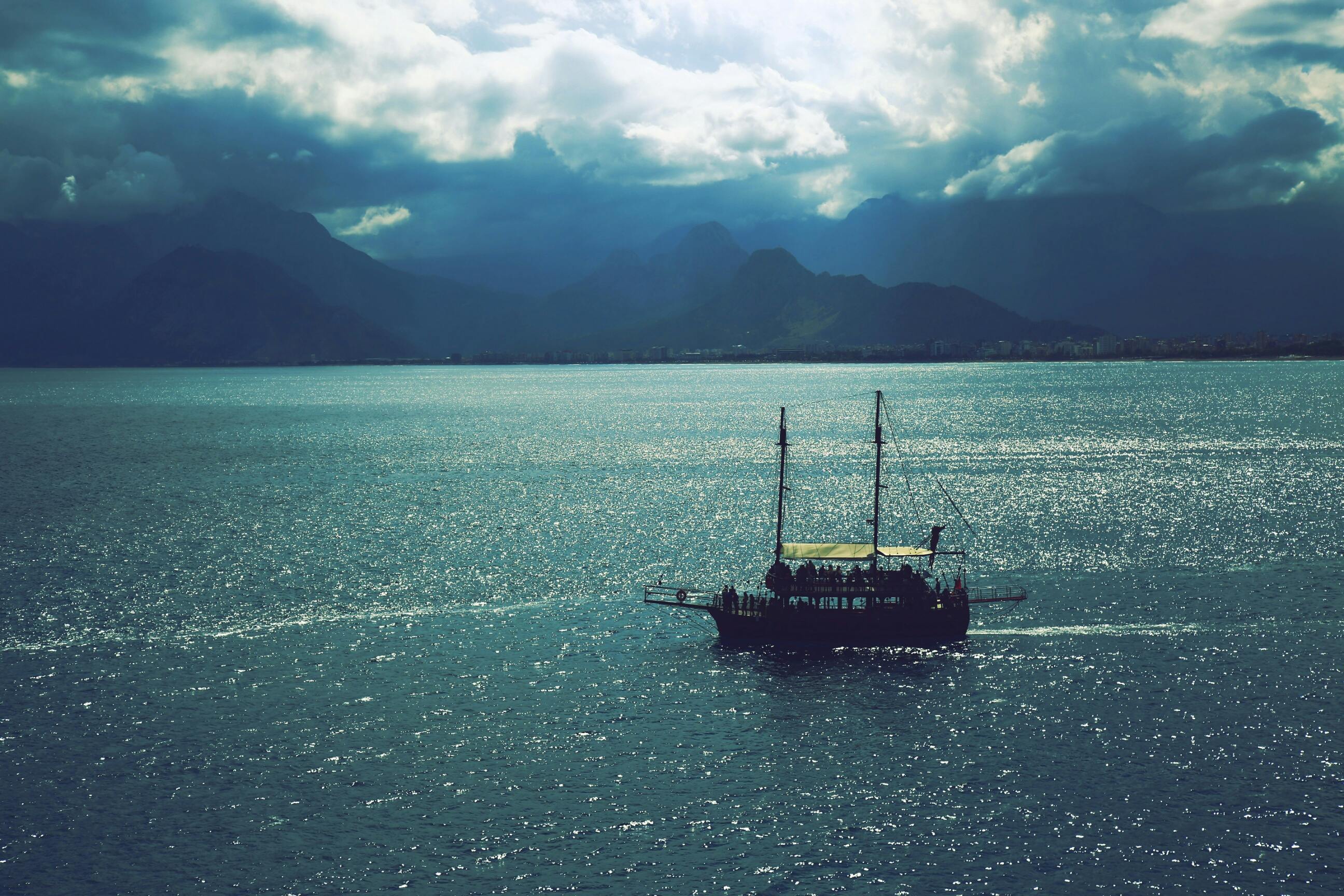 在戏剧性的天空下，一艘孤独的船映衬着令人惊叹的山脉，呈现出一片宁静的海景
