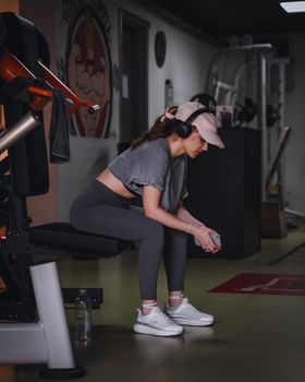 Woman in gym attire resting on a bench with headphones. Modern fitness lifestyle.