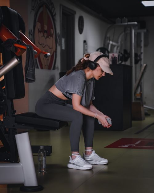 Free Woman in gym attire resting on a bench with headphones. Modern fitness lifestyle. Stock Photo
