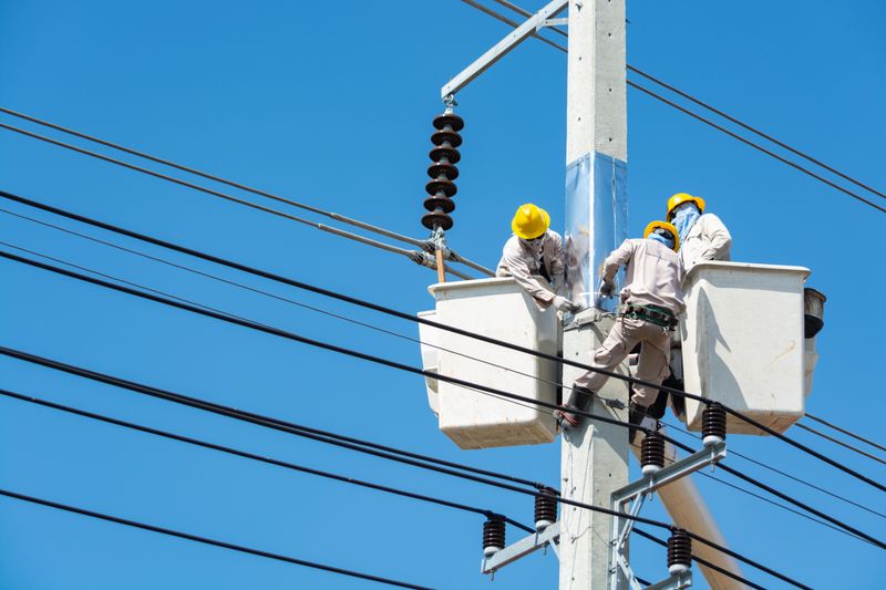 Utility workers in bucket lifts repairing overhead power lines