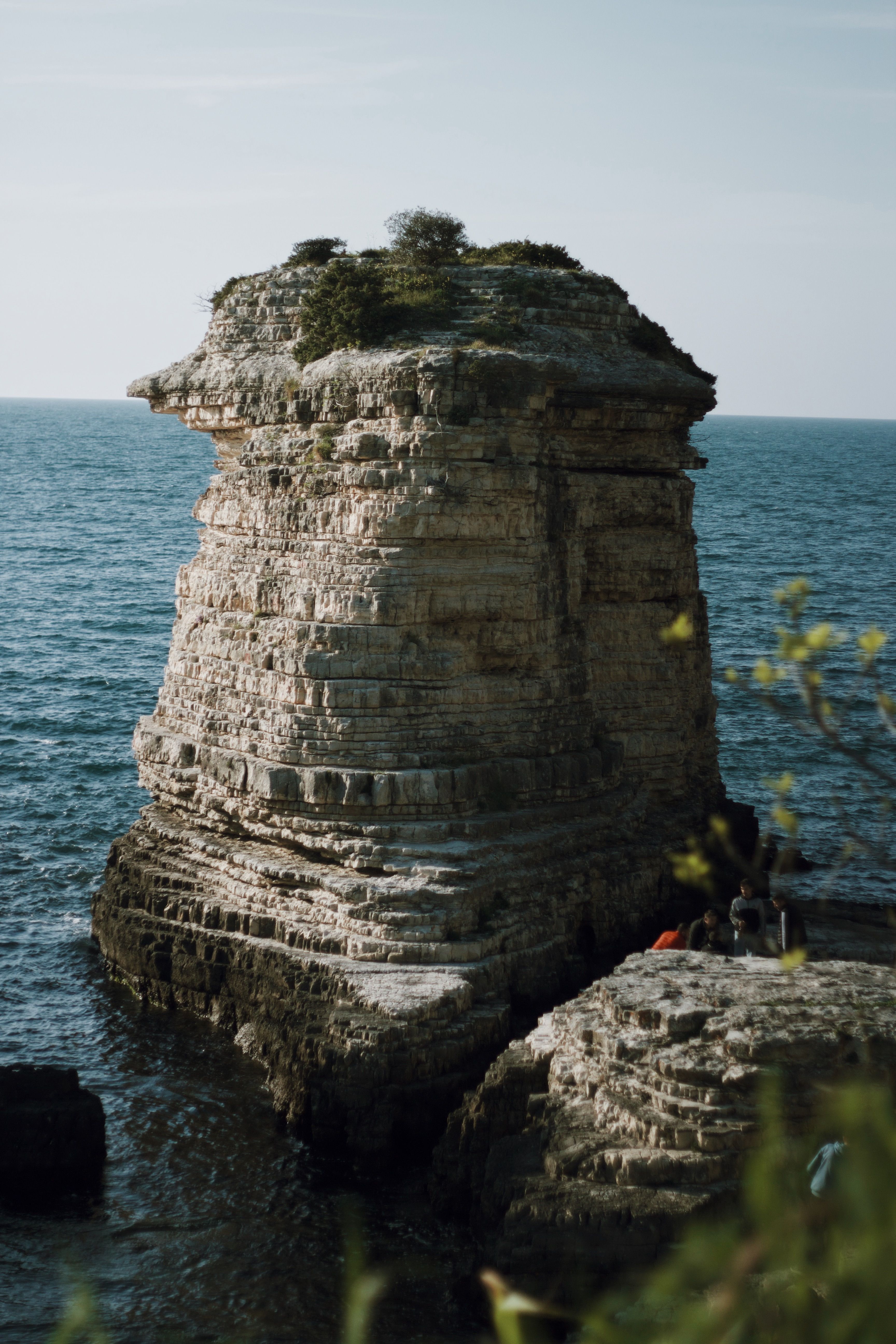 A stunning eroded rock formation along a serene coast, surrounded by the blue sea.