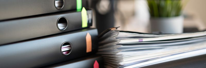 Stack of colorful ring binders and documents on a modern office desk setting.