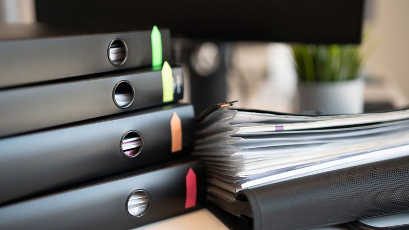 Stack of colorful ring binders and documents on a modern office desk setting.
