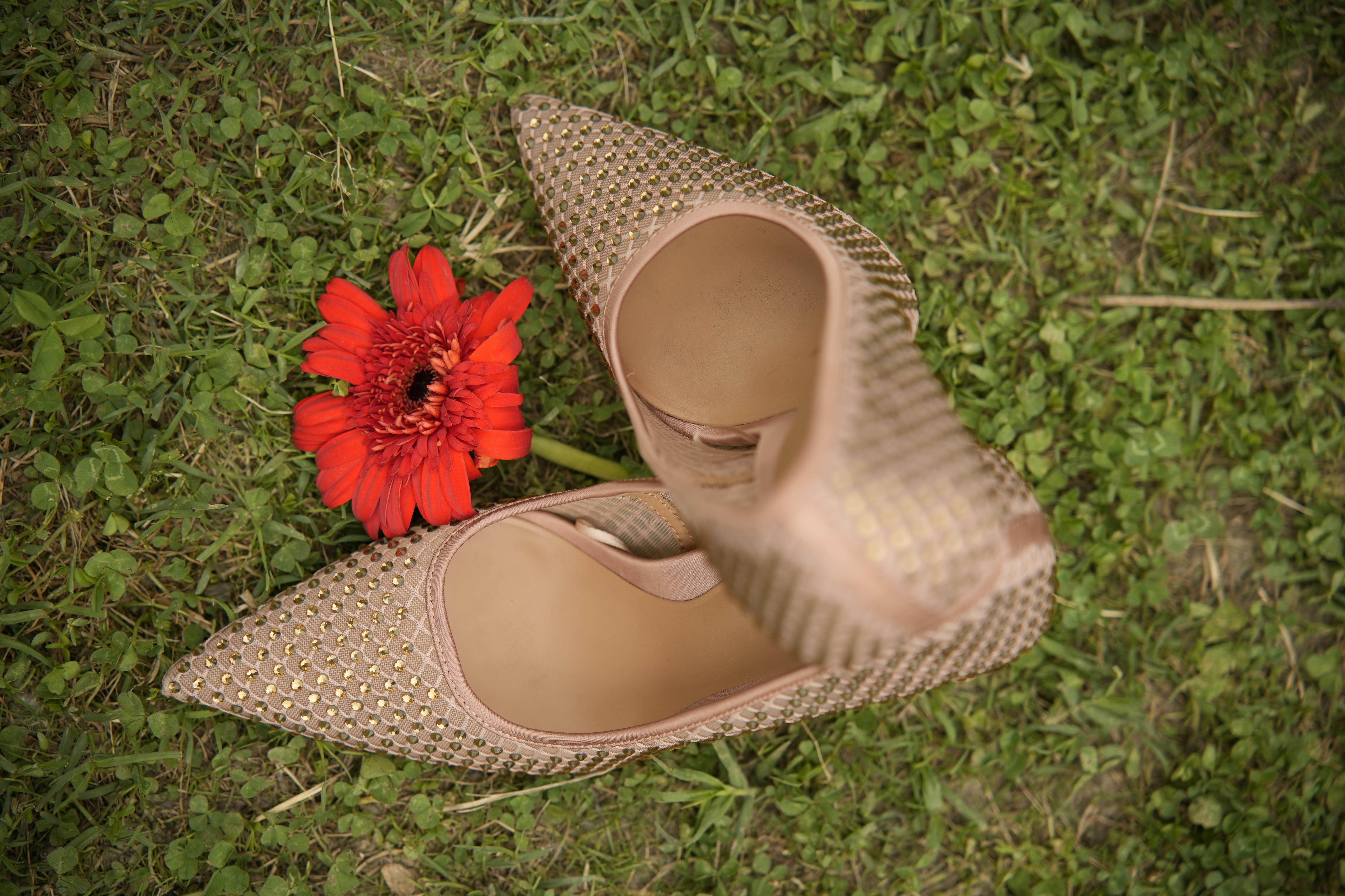 Stylish high heel shoes with a vibrant red flower on a lush grass background.