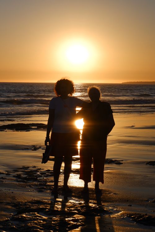 Free Two women silhouetted by a sunset, standing on a tranquil beach enjoying the serene ocean view. Stock Photo