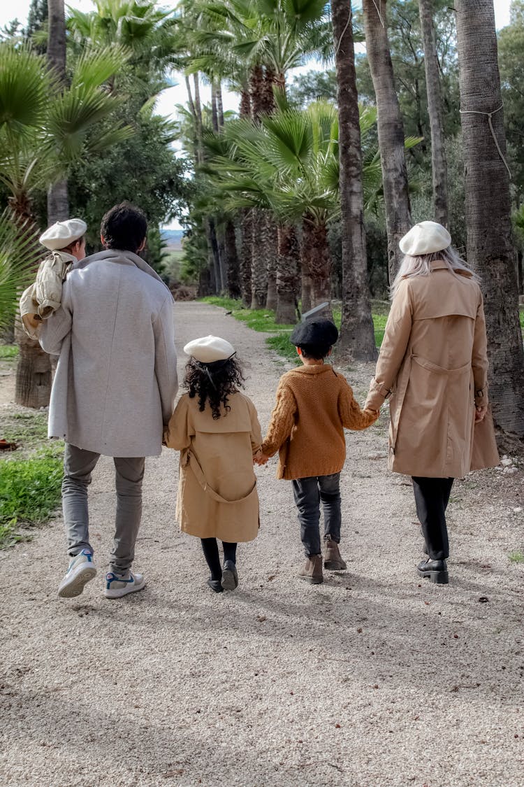 Family With Three Small Children In Berets Walking Down An Alley In A Palm Tree Park